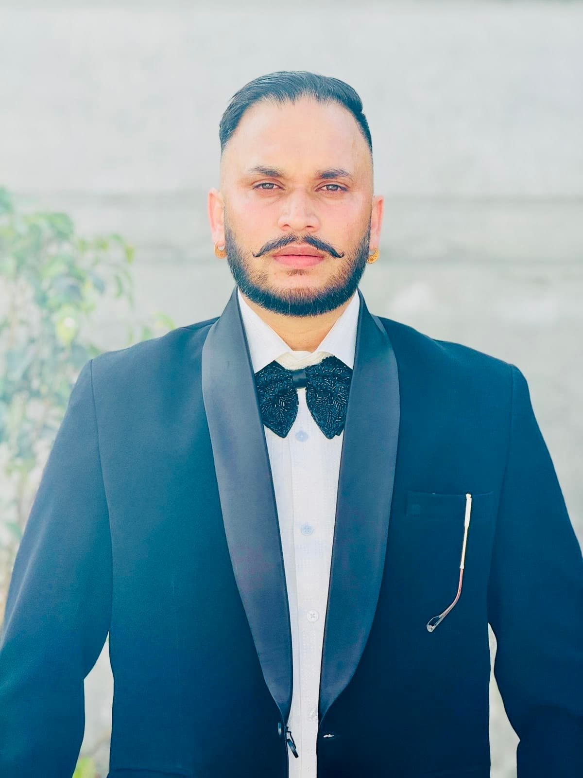 Man with a handlebar mustache and beard wearing a black tuxedo and bow tie.